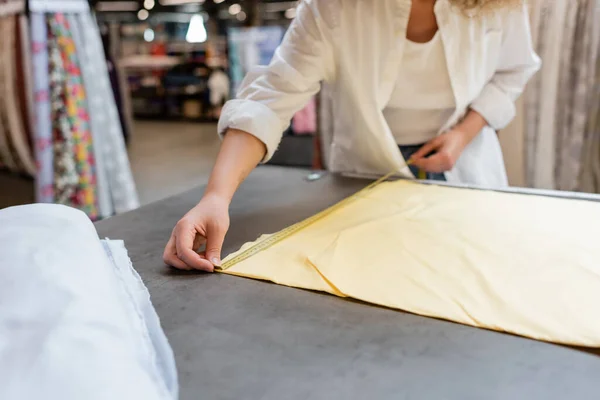 Vista recortada de la vendedora que mide el rollo de tela de lino amarillo en la tienda textil - foto de stock