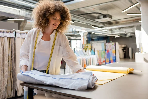 Glückliche Verkäuferin mit Maßband steht neben Stoffrollen im Textilgeschäft — Stockfoto