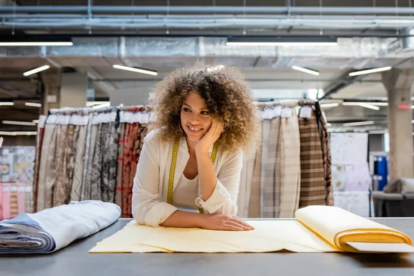 Glückliche Verkäuferin mit Maßband träumt in der Nähe von Stoffrollen im Textilgeschäft — Stockfoto
