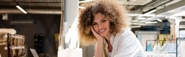 Happy saleswoman with curly hair smiling in textile shop, banner — Stock Photo