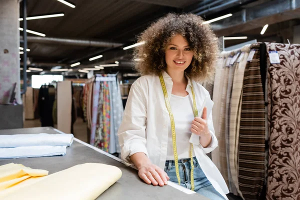 Positive saleswoman holding digital tablet near fabric rolls on desk in textile shop — Stock Photo