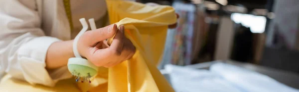Cropped view of salesperson with needle cushion on hand holding yellow fabric while working in textile shop, banner — Stock Photo