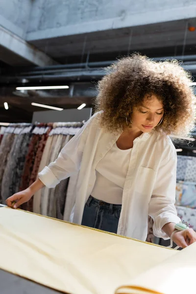Фігурна продавчиня з голкою подушкою на руці вимірює жовту тканину в текстильному магазині — стокове фото