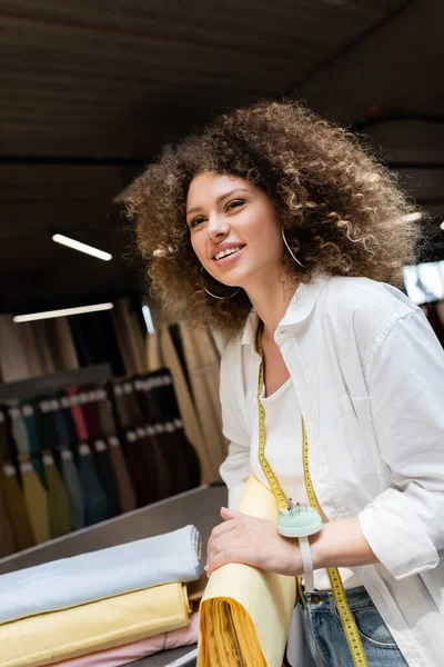 Verkäuferin mit Nadelkissen in der Hand hält gelbe Stoffrolle im Textilgeschäft — Stockfoto