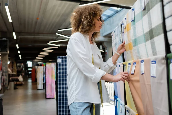 Curly saleswoman choosing among patterned fabric in textile store — Stock Photo