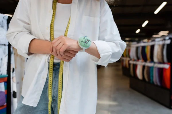 Vista recortada de la vendedora con cinta métrica y cojín de aguja a mano en la tienda textil - foto de stock