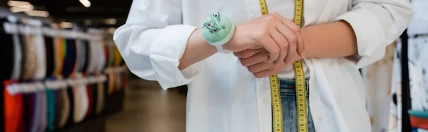Partial view of seller with measuring tape and needle cushion on hand in textile shop, banner — Stock Photo