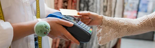 Cropped view of seller with needle cushion on hand holding credit card reader near customer in textile shop, banner — Stock Photo