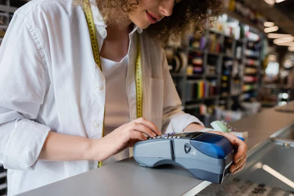 Cropped view of saleswoman working with payment terminal on counter in textile shop — Stock Photo