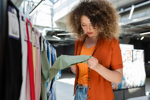 Кучерява жінка вибирає серед різних тканин у текстильному магазині — стокове фото