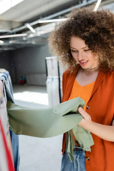 Mujer rizada sonriendo al elegir la tela en la tienda textil - foto de stock