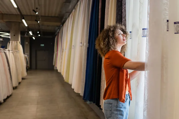 Young amazed woman choosing looking at different curtains in textile shop — Stock Photo