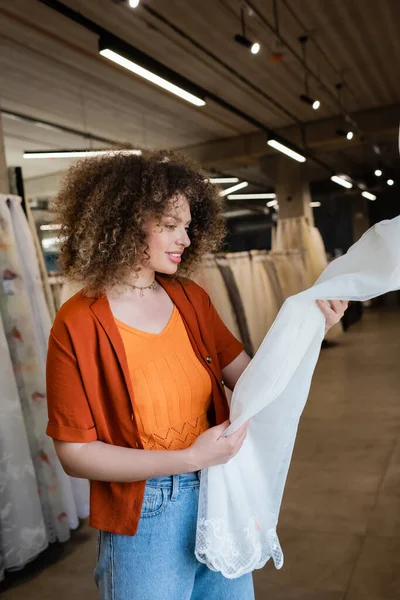 Positive woman looking at curtains in blurred textile shop — Stock Photo