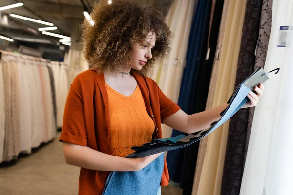 Comprador joven mirando muestras de tela en tienda textil borrosa - foto de stock