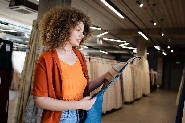 Young smiling woman holding fabric samples in blurred textile shop — Stock Photo