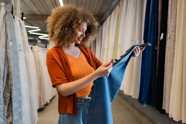 Curly customer smiling and looking at fabric samples in textile shop — Stock Photo