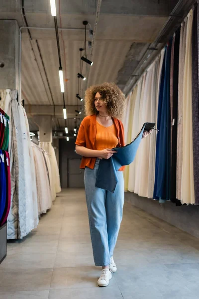 Jeune femme tenant des échantillons de tissu tout en marchant dans un magasin de textile — Photo de stock