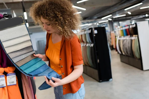Mujer rizada eligiendo tela de muestras en tienda textil - foto de stock