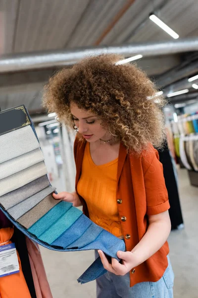 Jeune femme regardant des échantillons de tissu coloré dans un magasin de textile — Photo de stock
