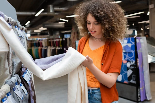 Кучерявий клієнт дивиться на іншу тканину в текстильному магазині — стокове фото