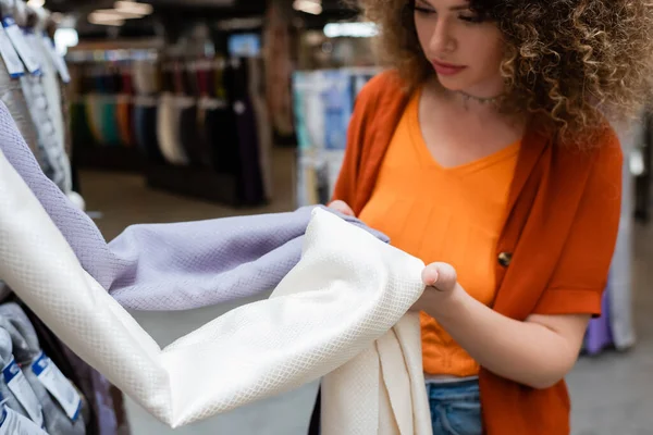 Розмитий фігурний клієнт тримає текстуровану тканину в текстильному магазині — стокове фото