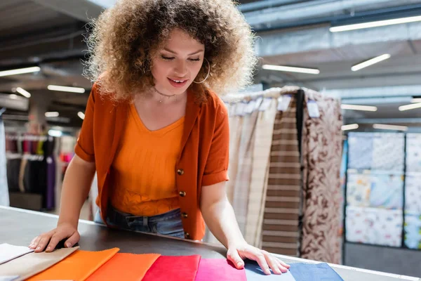 Cliente alegre olhando para amostras têxteis coloridas na mesa na loja — Fotografia de Stock
