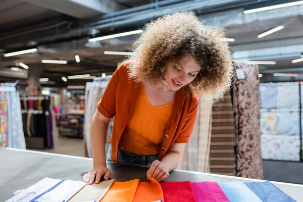 Positive buyer choosing cloth from colorful samples on table in textile shop — Stock Photo