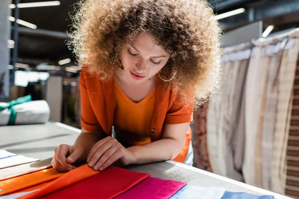 Jeune femme touchant différents échantillons de tissu dans une boutique de textiles — Photo de stock