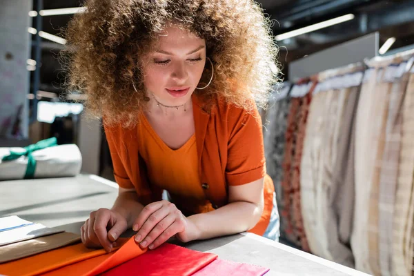 Curly client touching cloth samples on table in blurred textile shop — Stock Photo