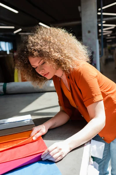 Curly customer holding colorful cloth samples near table in textile shop — Stock Photo