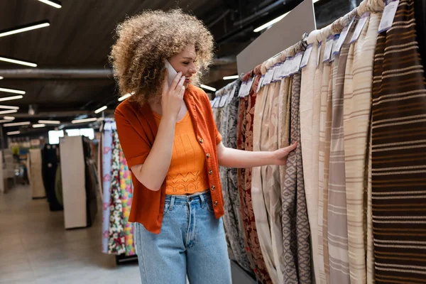 Positive Kunden berühren Tuch und sprechen auf Smartphone im Textilgeschäft — Stockfoto