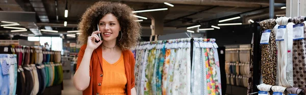 Веселая женщина разговаривает по мобильному телефону и смотрит прочь в текстильном магазине, баннер — стоковое фото
