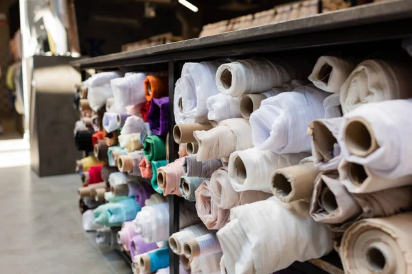 Diferentes rollos de tela en estantes en la tienda textil - foto de stock