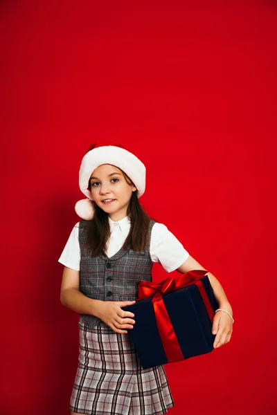 Задоволена дівчина в картатому жилеті і капелюсі Санта тримає подарункову коробку ізольовано на червоному — стокове фото