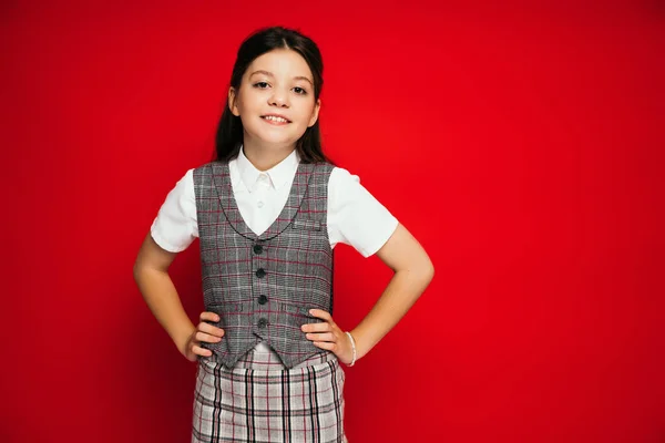 Cheerful child in plaid vest and skirt posing akimbo isolated on red, banner — Stock Photo