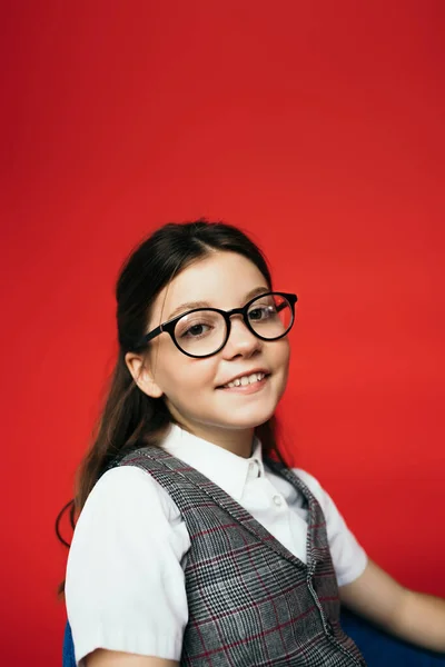 Ritratto di gioiosa ragazza bruna con gli occhiali che sorride alla telecamera isolata sul rosso — Foto stock