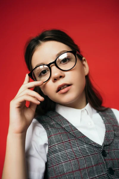 Retrato de niña preadolescente en gafas de moda posando y mirando a la cámara aislada en rojo - foto de stock