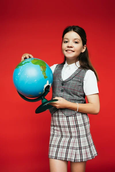 Menina sorridente em colete xadrez e saia segurando globo isolado em vermelho, bandeira — Fotografia de Stock