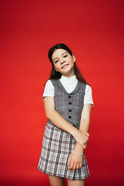 Brunette girl in plaid vest and skirt looking at camera isolated on red, banner — Stock Photo