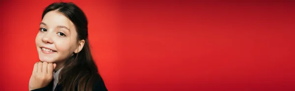 Portrait de fille brune souriante avec la main près du menton regardant la caméra isolée sur rouge, bannière — Photo de stock