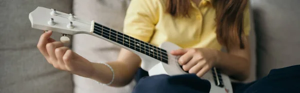 Vista cortada de criança desfocada afinação pequena guitarra havaiana em casa, banner — Fotografia de Stock