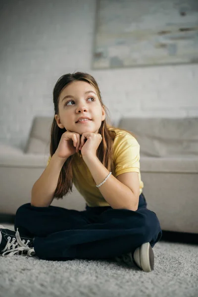 Smiling and dreamy girl sitting on floor with crossed legs and looking away — Stock Photo