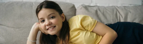 Веселая девушка отдыхает на диване дома и улыбается в камеру, баннер — стоковое фото