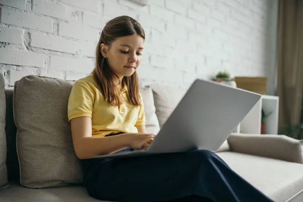 Брюнетка дівчина використовує ноутбук, сидячи на дивані у вітальні — Stock Photo