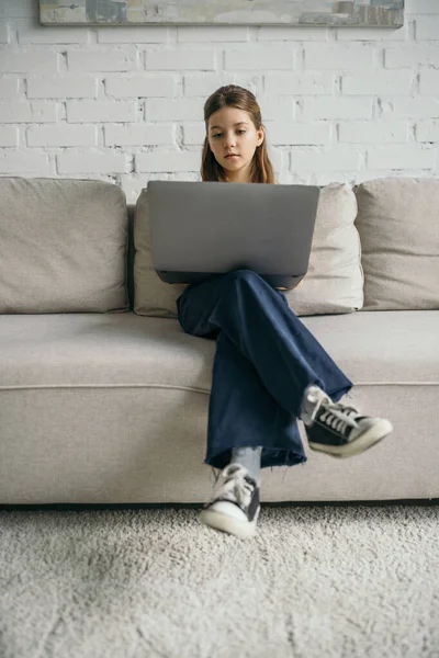 Frühchen Mädchen mit Laptop sitzt auf moderner bequemer Couch zu Hause — Stockfoto