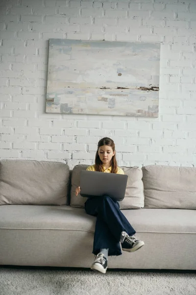 Brünettes Mädchen mit Laptop sitzt auf gemütlicher Couch im Wohnzimmer — Stockfoto