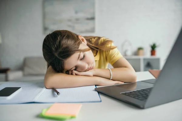 Tired child sleeping near copybook and laptop with smartphone on table at home — Stock Photo