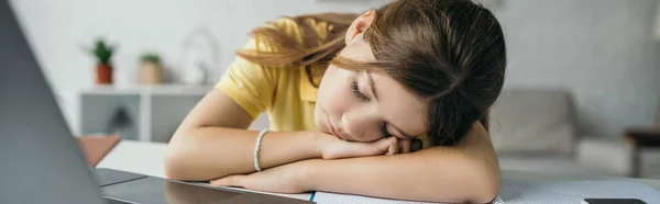 Tired schoolgirl sleeping near blurred laptop at home, banner — Stock Photo