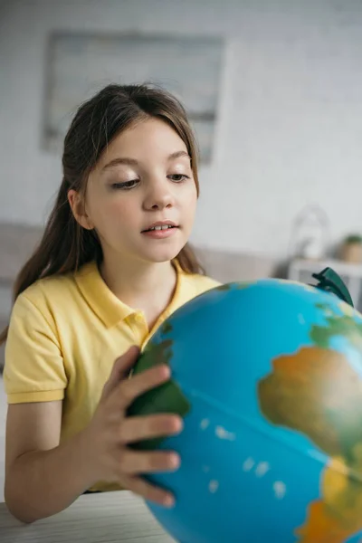 Preteen schoolgirl looking at blurred globe and learning geography at home — Stock Photo