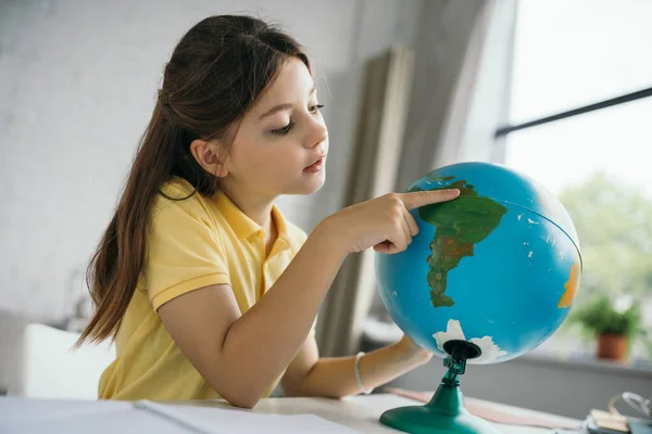 Preteen schoolgirl pointing at globe while learning geography at home — Stock Photo